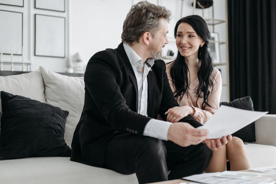 Couple smiling while sitting on a couch reviewing documents indoors.
