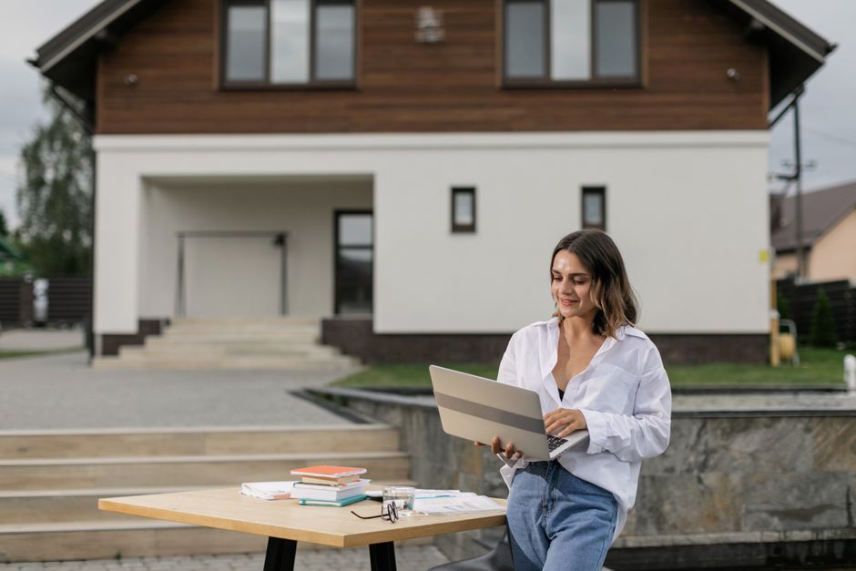 Woman in casual attire using a laptop outdoors at a table with books.